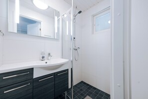 Uma casa de banho moderna com uma pia branca, gavetas escuras, cabine de duche em vidro e uma janela com persianas.
