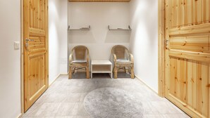 A room with wooden doors, two wicker chairs, a small table, and a grey rug. - 3BR Holiday Apt. with Sauna (Kittilä)