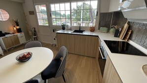 Une cuisine moderne dotée d’un îlot central, d’un coin repas avec une table ronde et des chaises, et offrant une vue sur la ville grâce à de grandes fenêtres.
