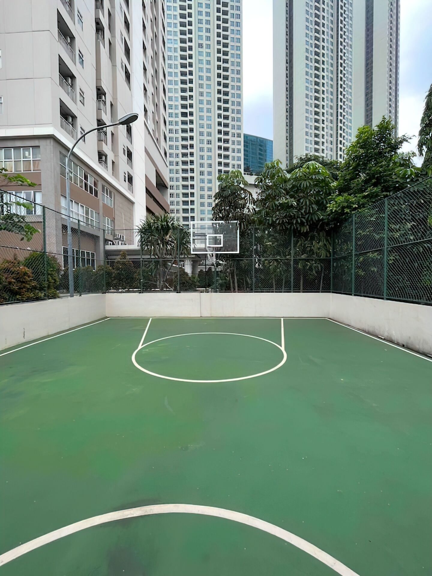 Una cancha de baloncesto al aire libre rodeada de edificios altos y zonas verdes.