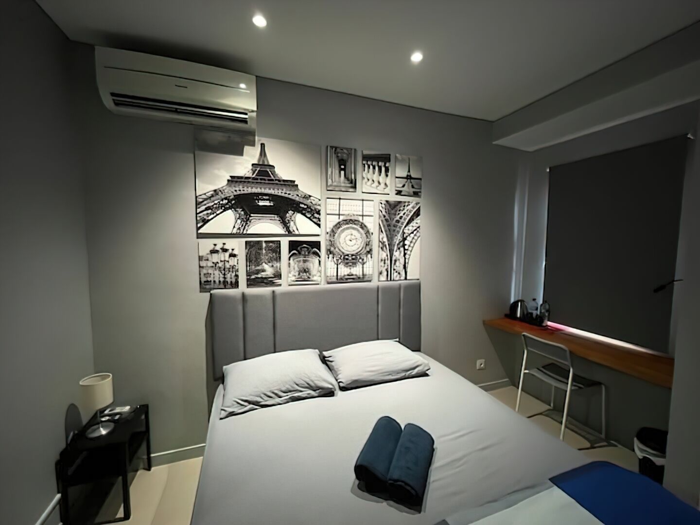 A modern hotel room with a bed, a desk, and a wall decorated with black and white photographs.