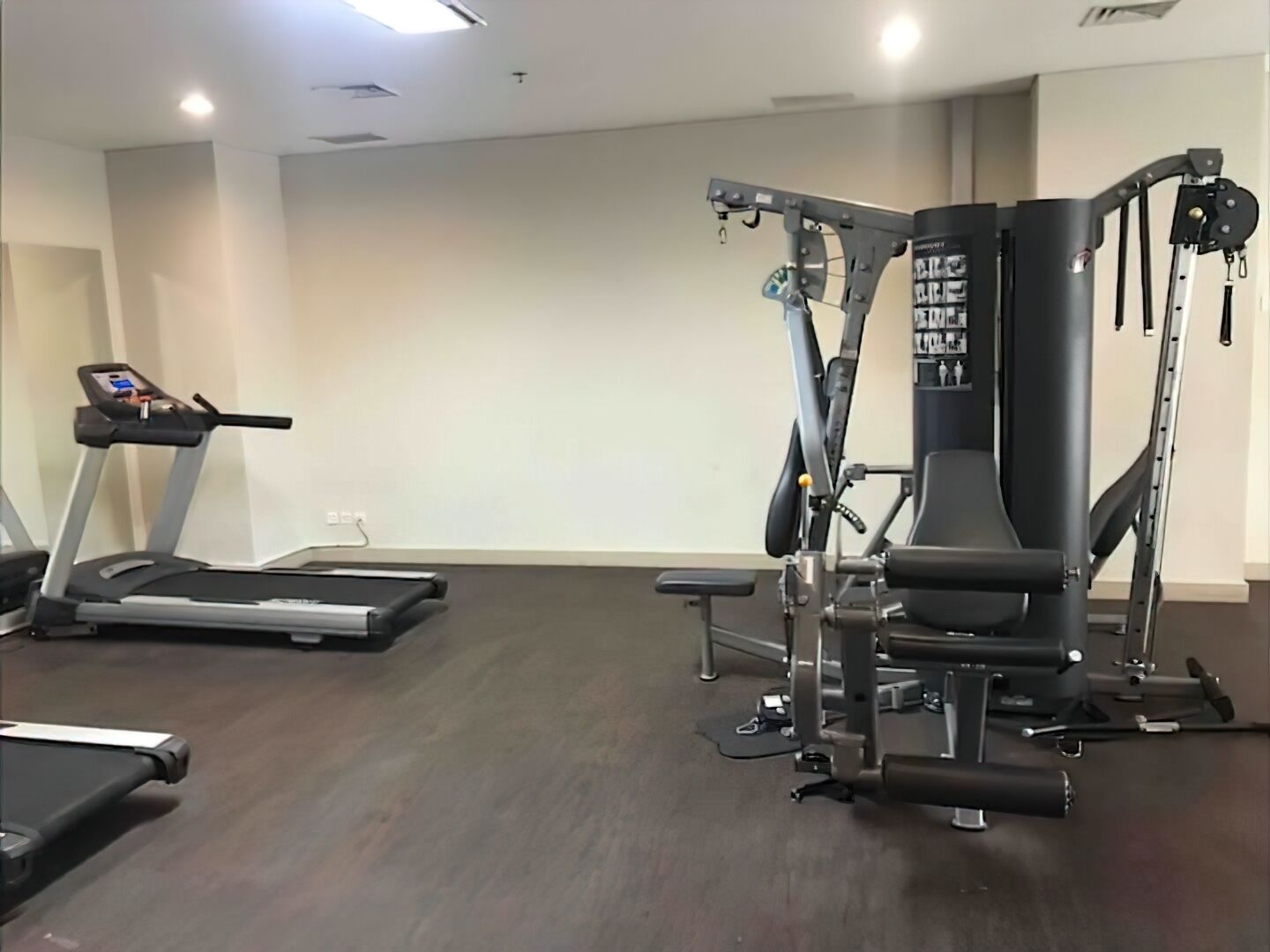 Un gimnasio con cinta de correr, máquinas de pesas y una banca.