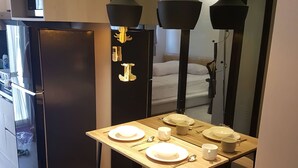 Kompakti hotellihuone, jossa on pieni keittiönurkkaus, ruokapöytä, jossa on lautaset ja aterimet, keltainen nojatuoli ja peili, joka heijastaa huonetta.