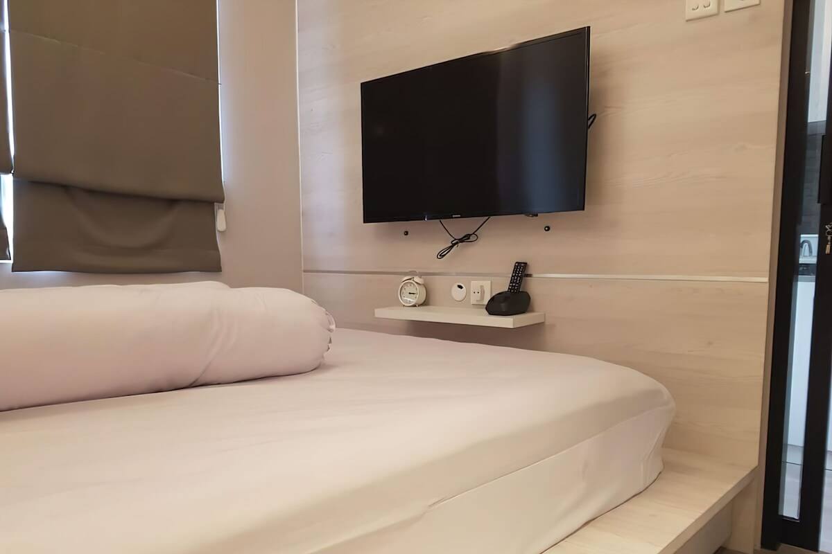 A modern bedroom with a bed, a mounted TV, a bedside table with a clock, and a power outlet.
