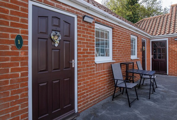 A brick building with a brown door, a window, and a patio area with a table and chairs. - The Angel Inn – Pub, Dine & Stay Misson (Misson)