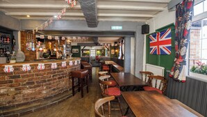 Eine Kneipe mit Ziegelwand, Holztischen und roten Sitzhussen. Eine Union-Jack-Flagge schmückt die Wand.