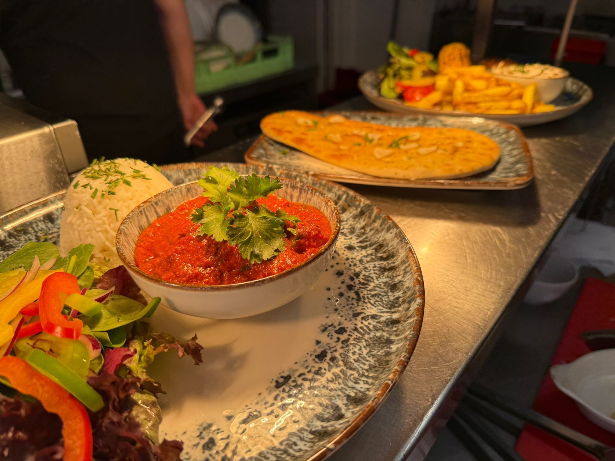 A dining table with a plate of food, including rice, a bowl of red sauce, and a salad.