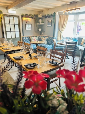Ein Restaurantinneres mit Holztischen, die zum Essen gedeckt sind, einer blauen Blumsofa und einer Wand mit einer Statue.
