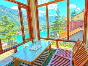 A room with a wooden table and bench, large windows offering a mountain view. - Hotel Alpine Manali (Manali)