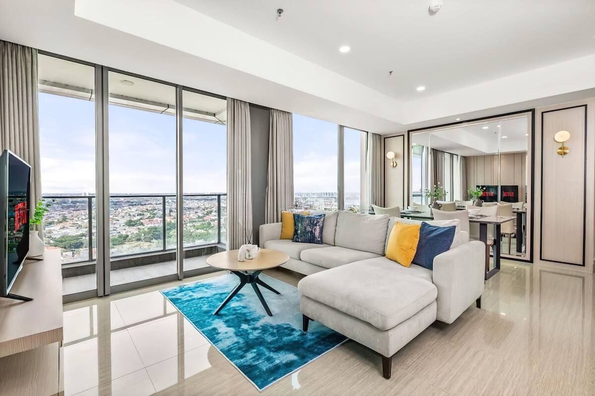 A modern living room with a large sofa, a coffee table, and a view of a cityscape through floor-to-ceiling windows.