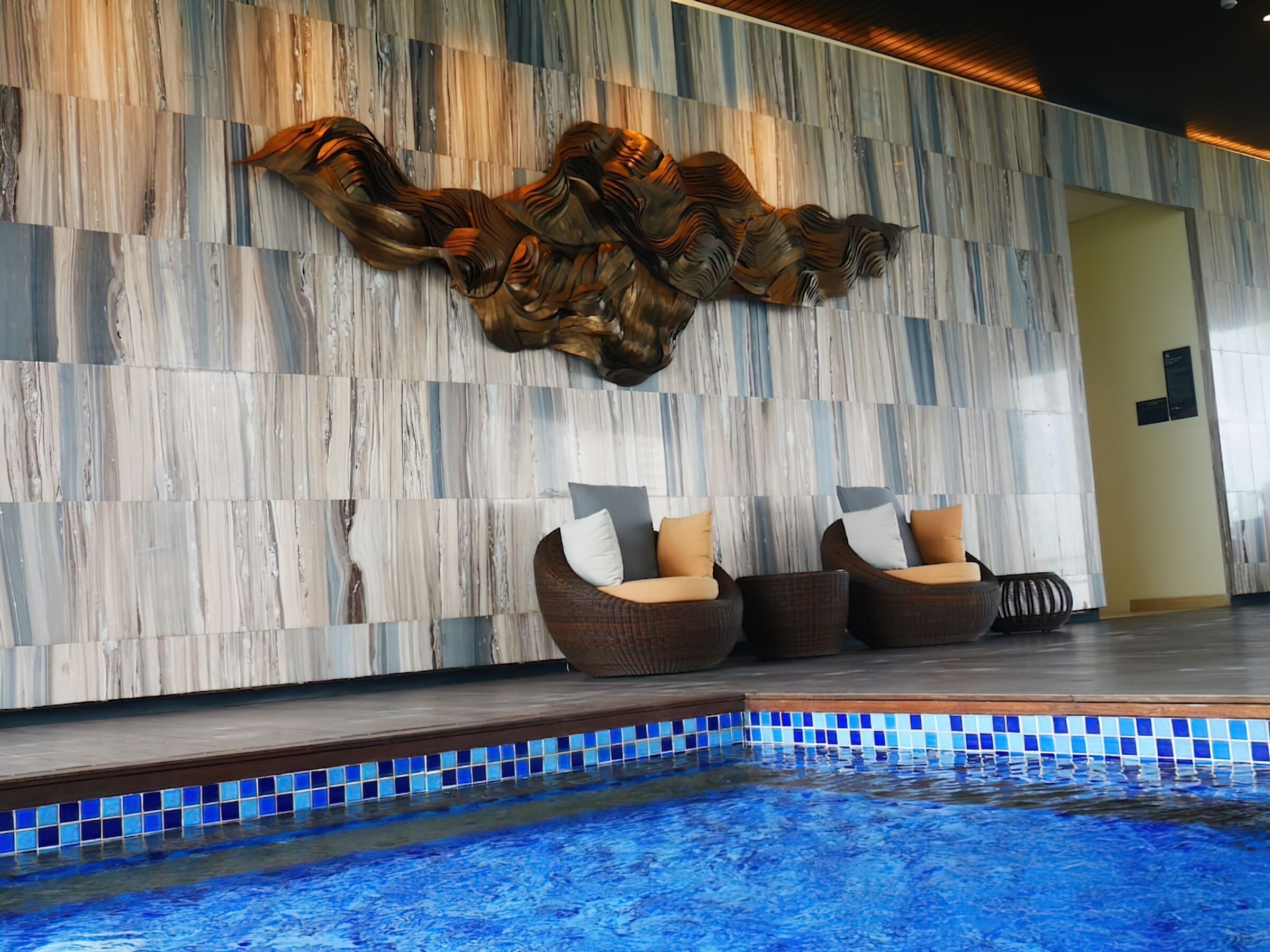 A pool area with a marble wall and a large decorative piece above the seating area.