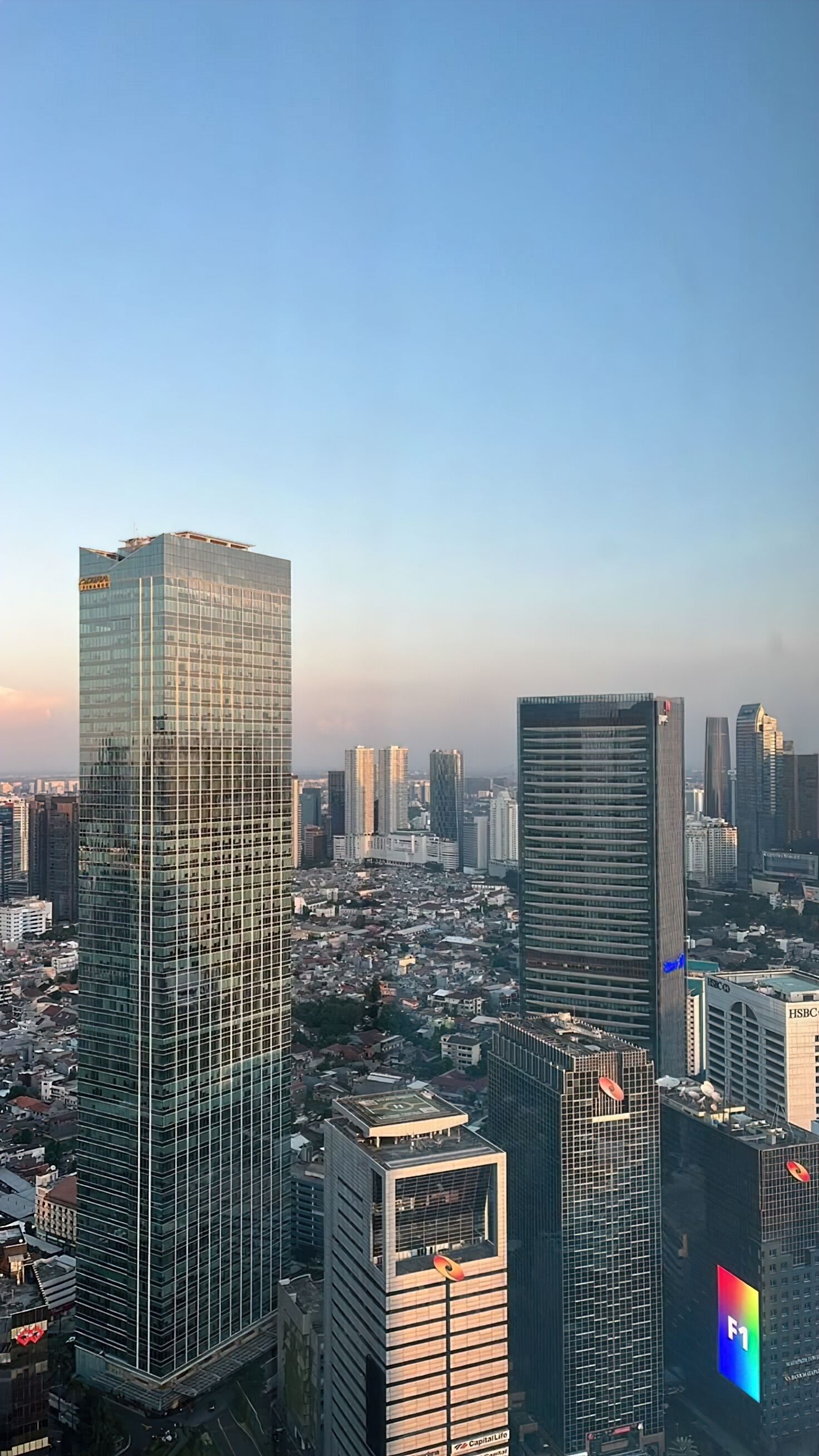 A cityscape with modern high-rise buildings, including a prominent glass skyscraper and a building with a distinctive red and white logo.