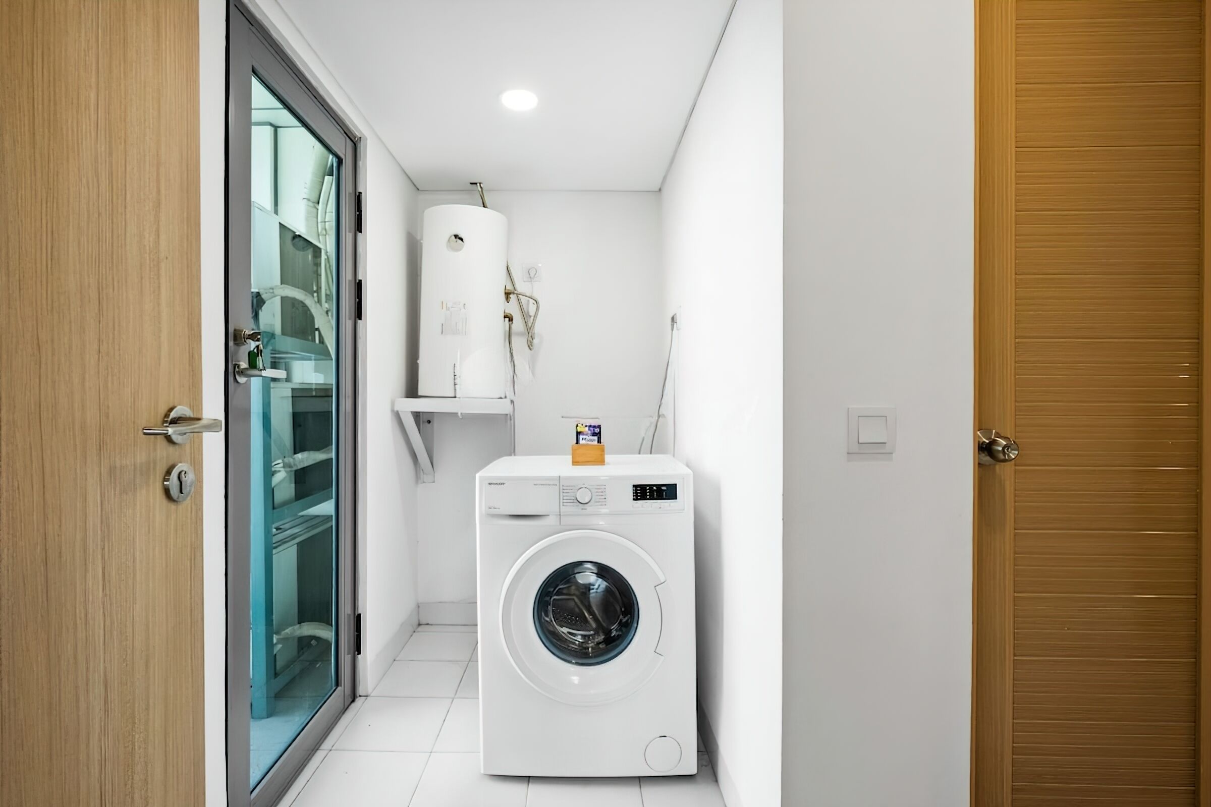 Een kleine wasruimte met een voorlader wasmachine, een glazen deur en een witte handdoekhouder.