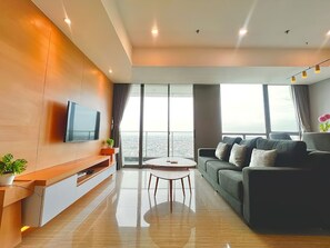 Un salon moderne avec une grande fenêtre, un téléviseur à écran plat, un canapé, une table basse et une plante.
