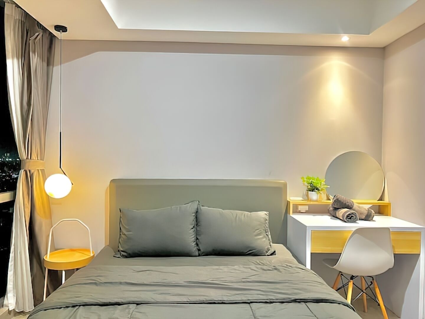 A modern bedroom with a bed, bedside table, chair, desk, and a hanging lamp.