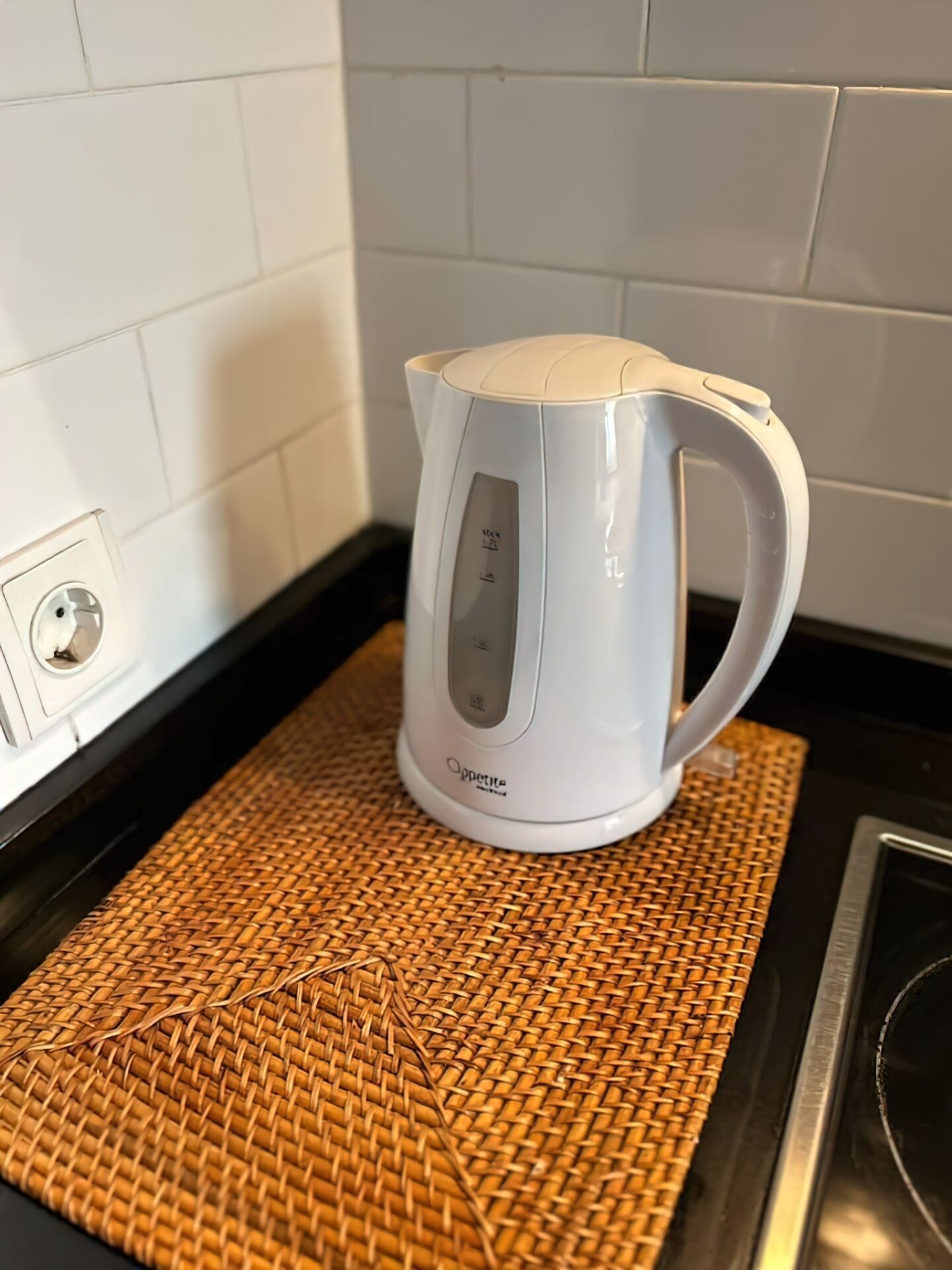 En vit vattenkokare för elanslutning står på en vävd bordsduk på en köksbänk.