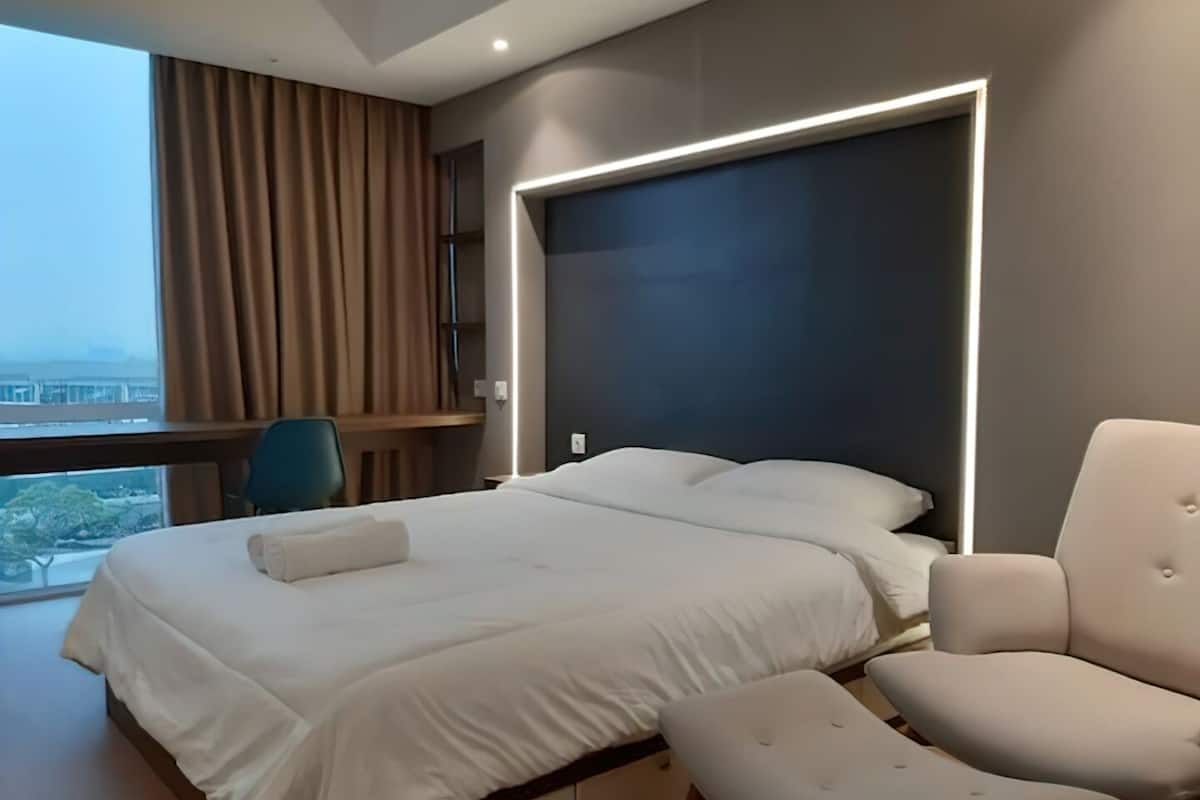 A modern hotel room with a large bed, a desk, and a view of the city.