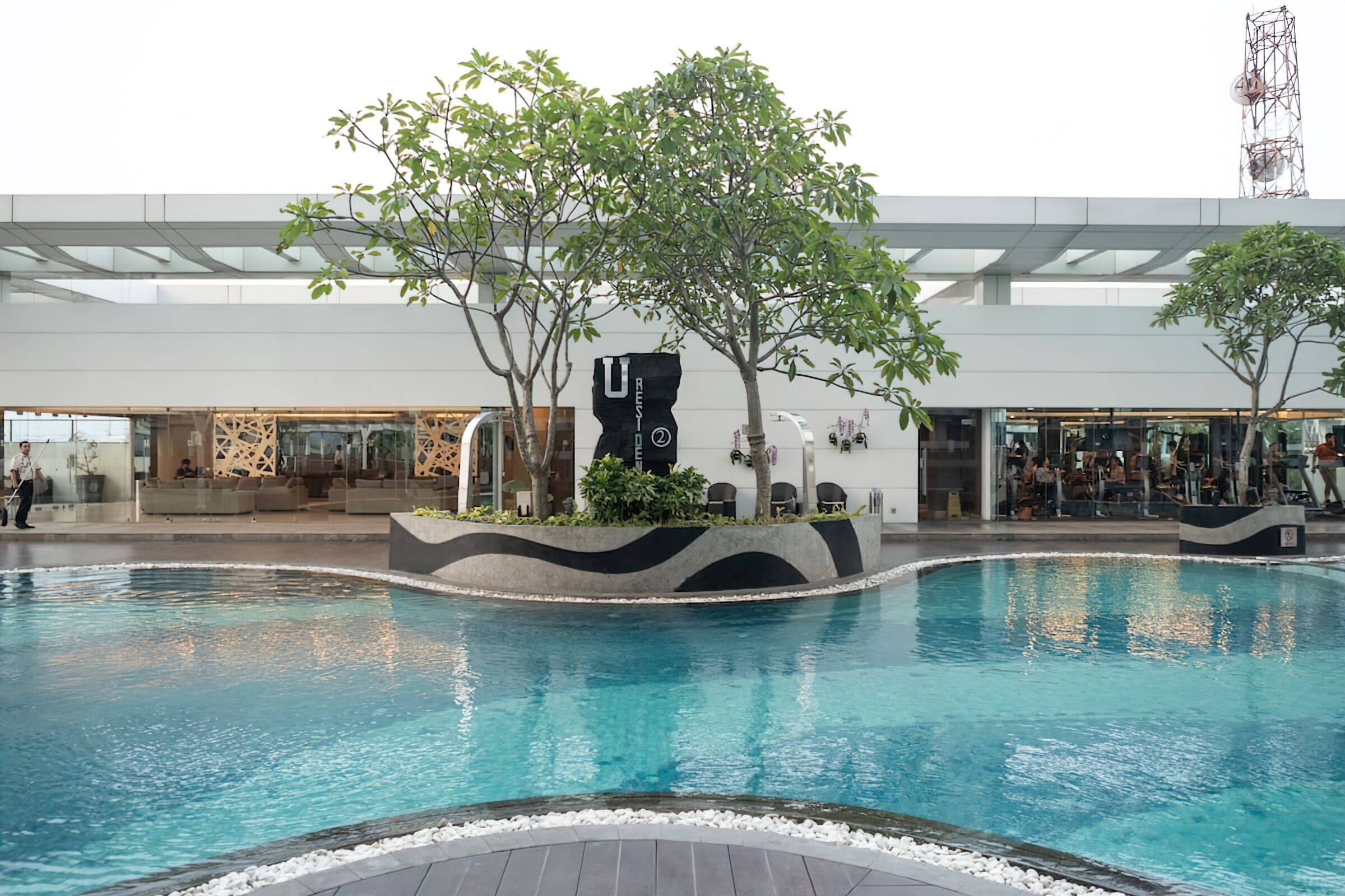 A modern indoor pool area with a central island, surrounded by seating and greenery.