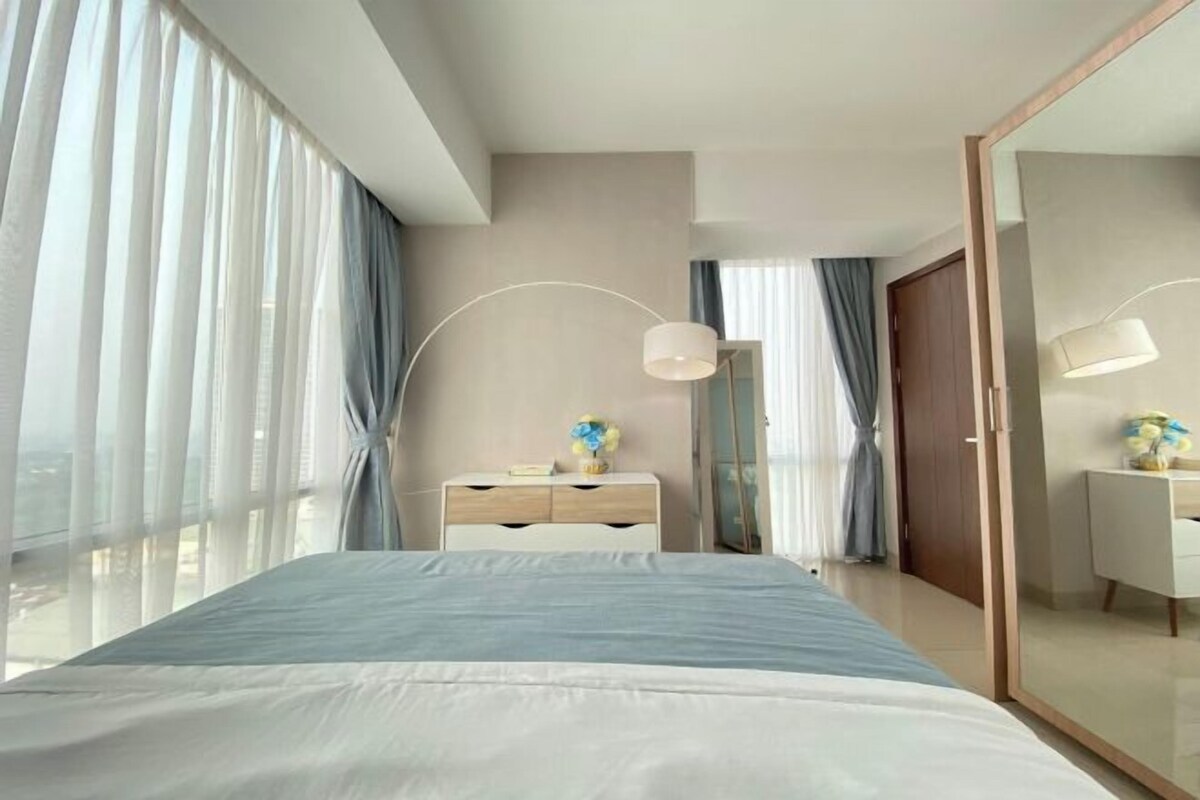 Habitación de hotel moderna con una cama grande, una mesita de noche, un espejo y vistas a la ciudad.