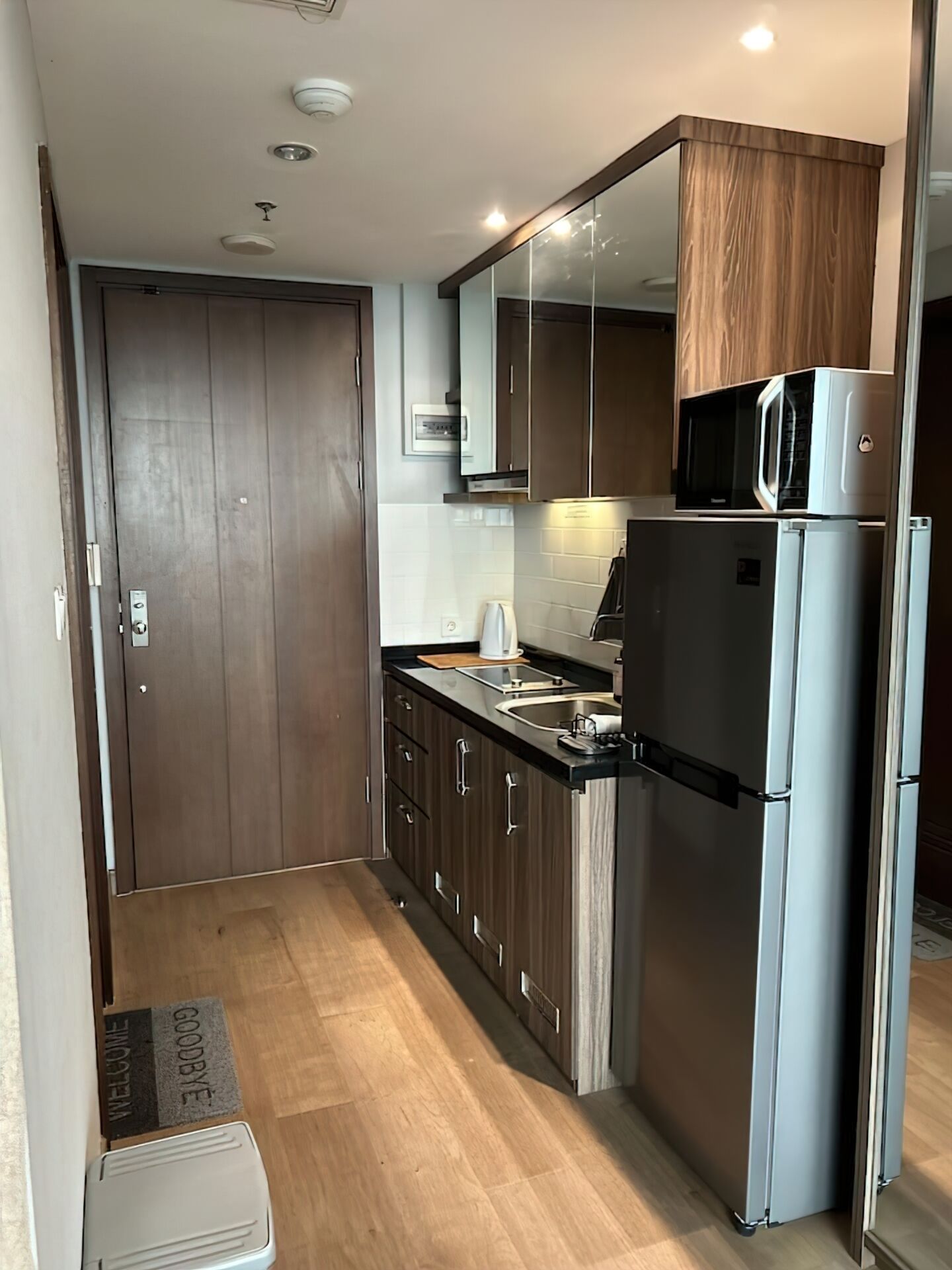 Eine kleine Küche mit Holzausstattung, einem Edelstahlkühlschrank, einer Mikrowelle und einem Spülbecken.