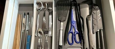 Un cassetto pieno di utensili e attrezzi da cucina, tra cui bacchette, coltelli, cucchiai, una spatola, pinze e forbici.