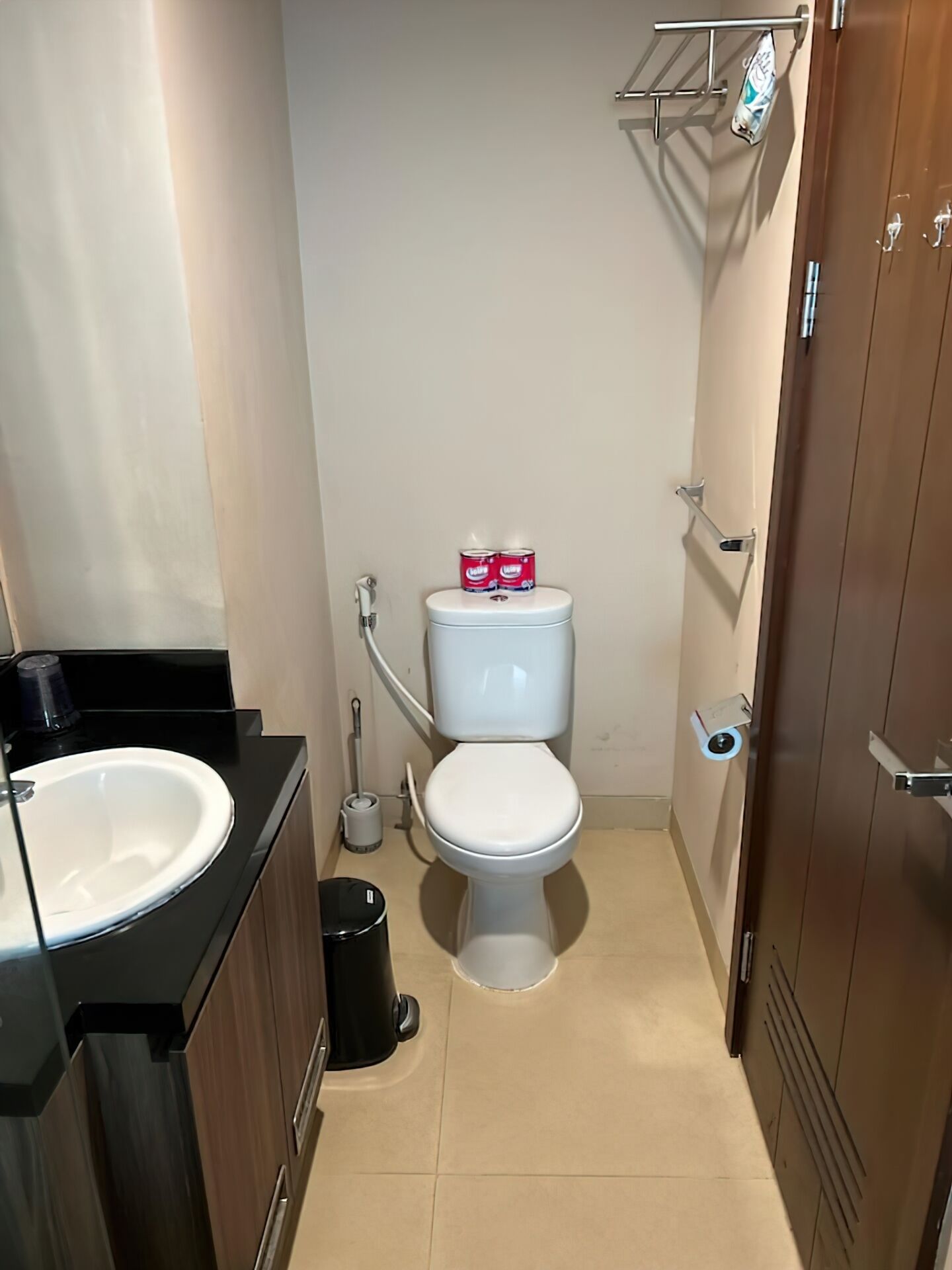 A compact bathroom with a white toilet, a black sink, and a trash bin.