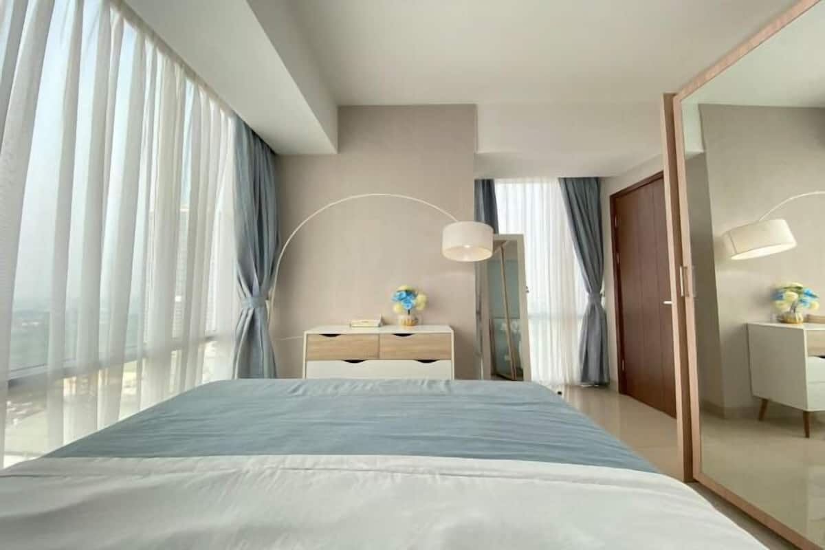 A modern hotel room with a large bed, a bedside table, a mirror, and a view of the city.