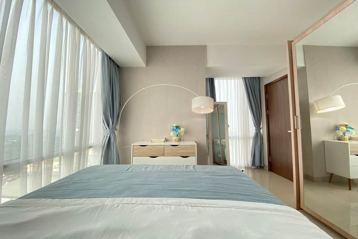 A modern hotel room with a large bed, a desk, and a wardrobe.
