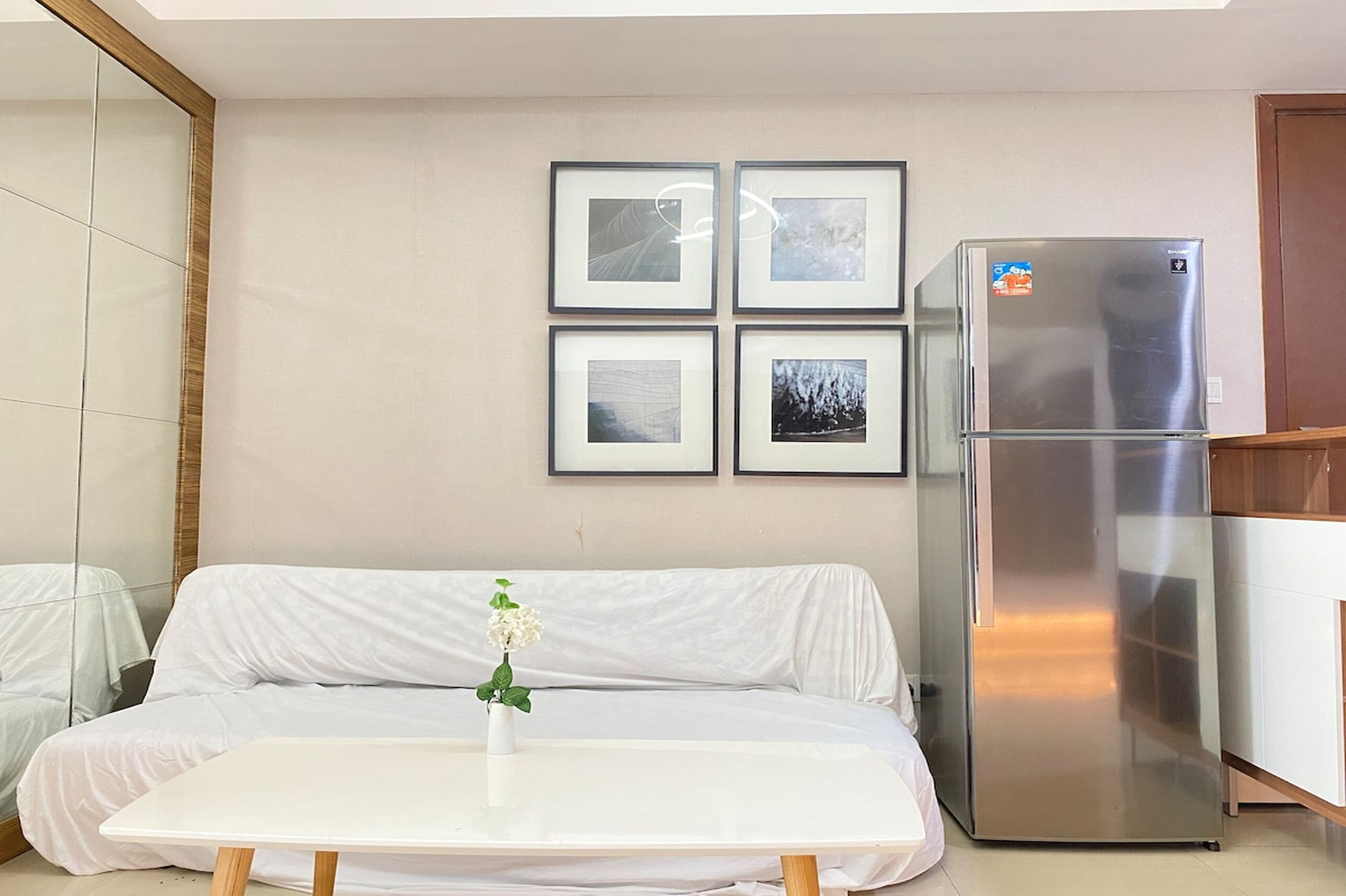 A modern kitchen with a stainless steel refrigerator, a white sofa, and a small table with a vase of flowers.