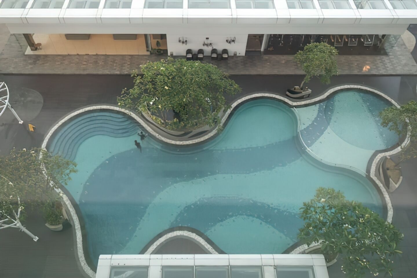 Vista aérea de un edificio moderno con un diseño de piscina único, con varias piscinas interconectadas y abundante vegetación.