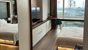 Una moderna camera d'albergo con due letti, una scrivania, una sedia e un'ampia finestra vista città.