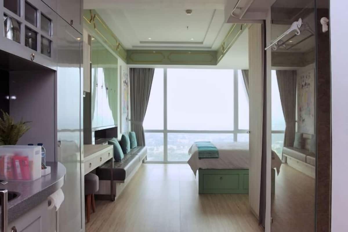 A modern bedroom with a large window, a bed, a desk, and a seating area.