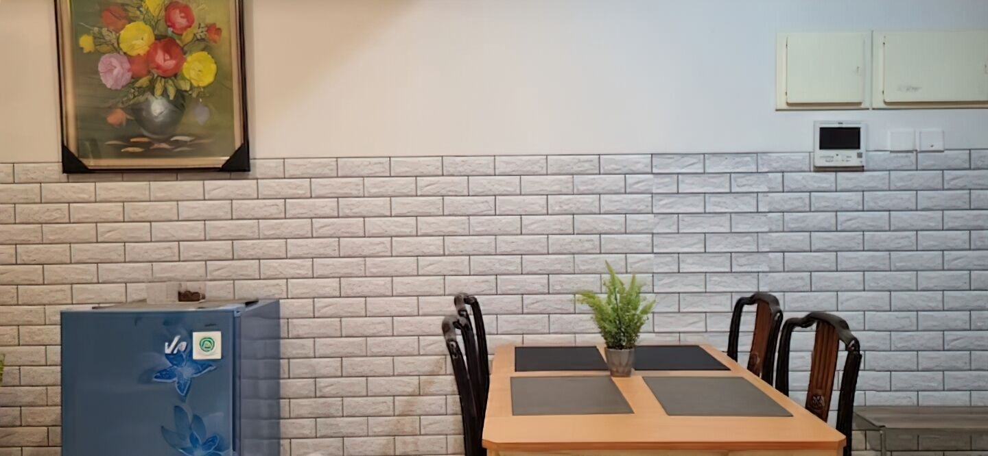Een eethoek met een bakstenen muur, een bloemschilderij, een koelkast en een tafel met stoelen.