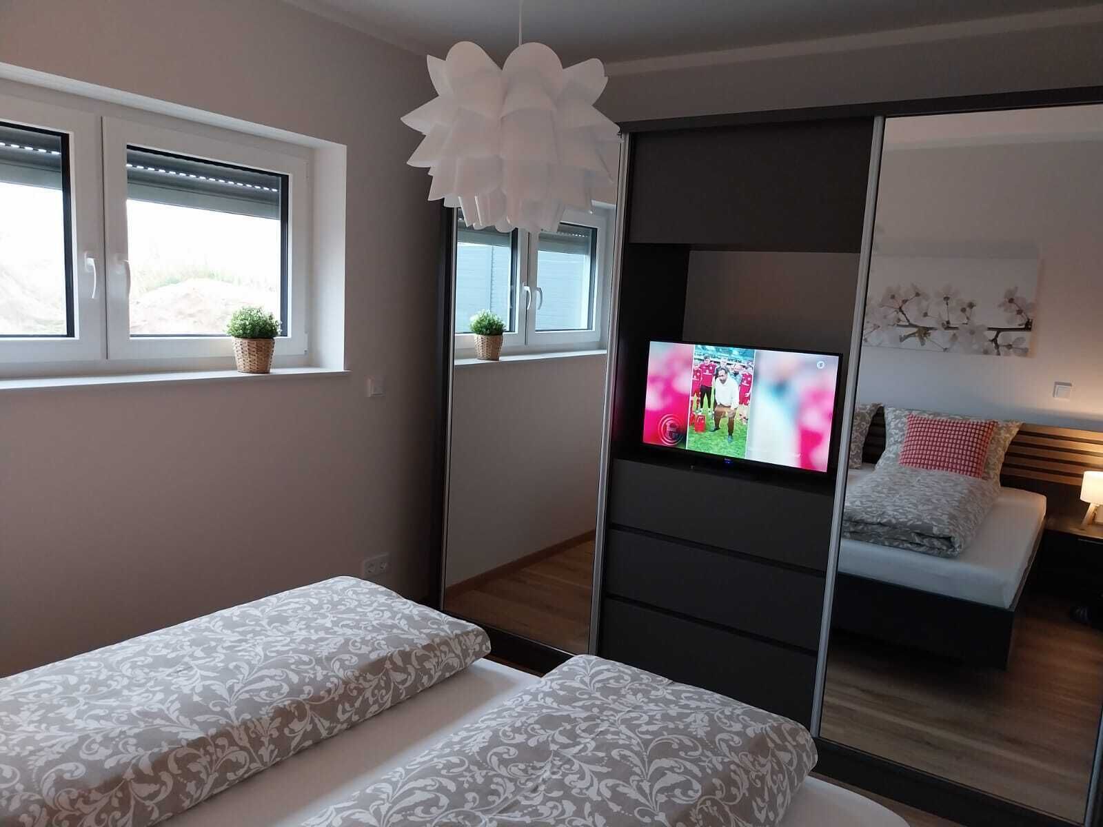 A modern bedroom with a bed, a TV, and a window with blinds.
