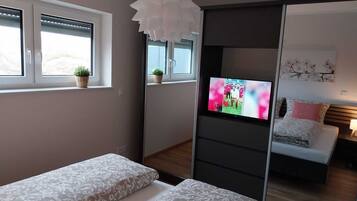 A modern bedroom with a bed, a TV, and a window with blinds.