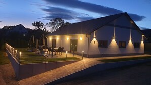 A modern house with a covered patio, outdoor seating, and a well-lit exterior at dusk.