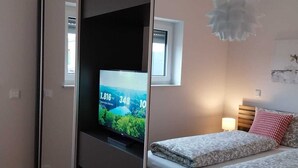 A bedroom with a bed, a TV on a sliding door, a window, and a ceiling light.