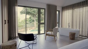 A modern bedroom with a large window, a bathtub, a black chair, and a wooden stool. - New, stylish, 3 bedroom home, with infinity pool and Table Mountain views (Cape Town)
