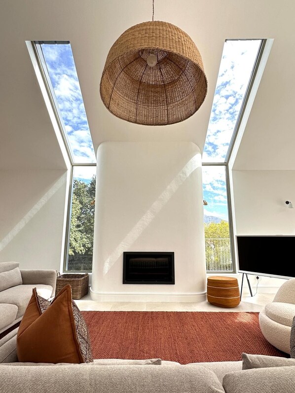 A modern living room with a fireplace, large windows, and a hanging light fixture.