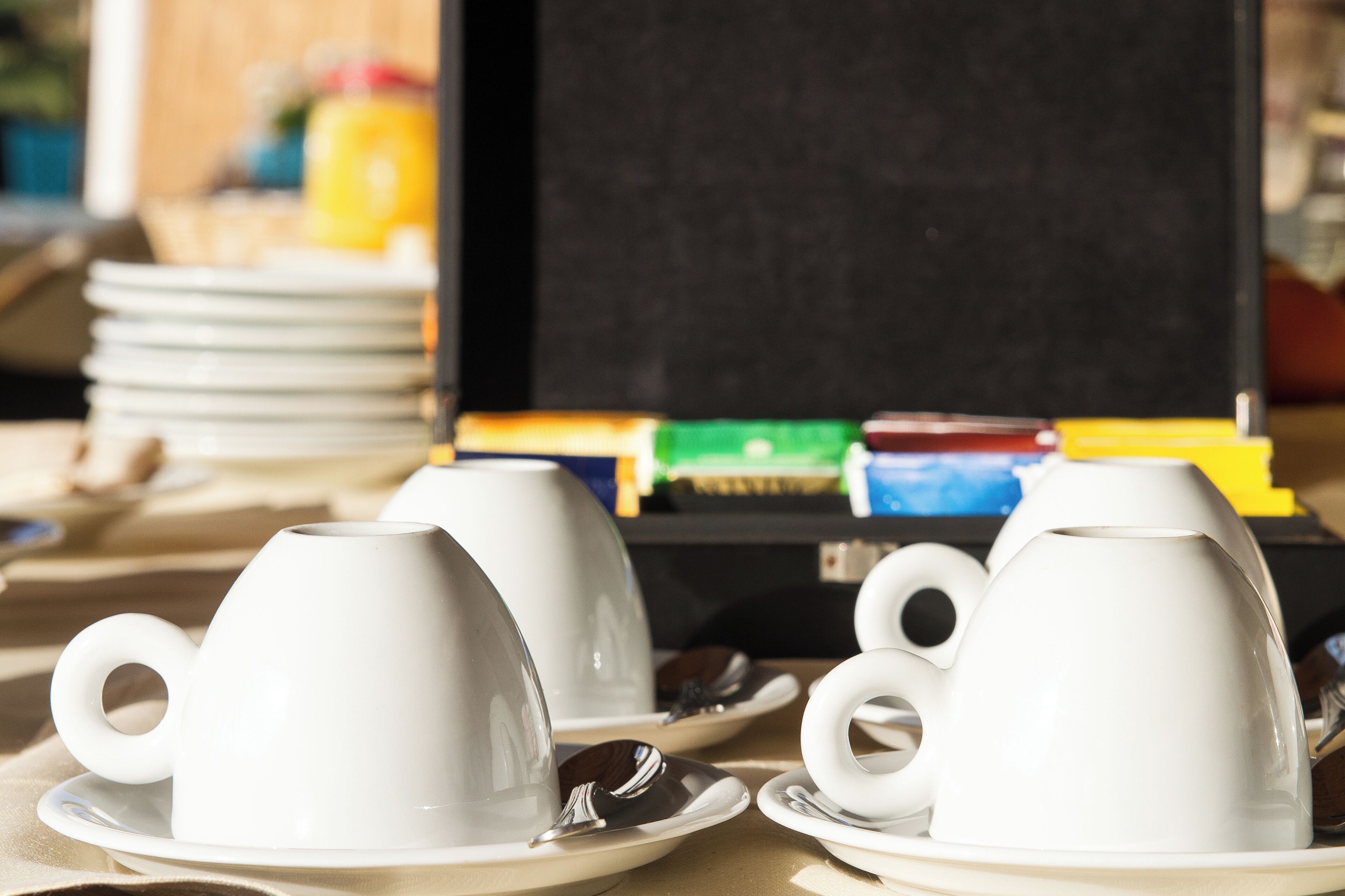 Two white ceramic cups on saucers, a stack of plates, and a blackboard in the background.