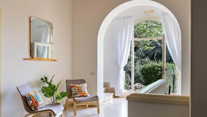 Un intérieur moderne avec une grande fenêtre en arc de cercle, un miroir, deux fauteuils ornés de coussins colorés et une plante en pot.