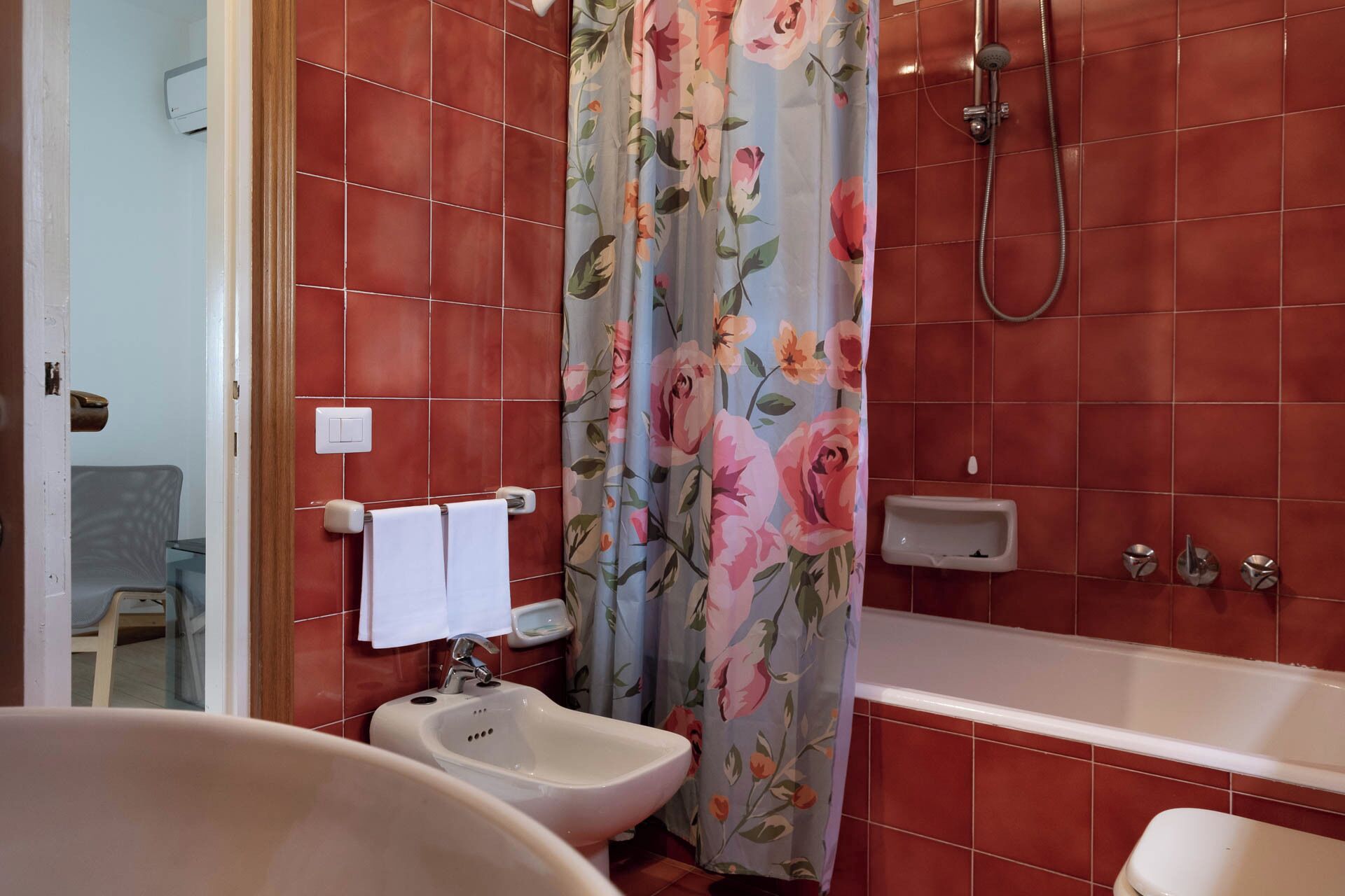 Een badkamer met rode tegels, een bidet, een badkuip en een douche.