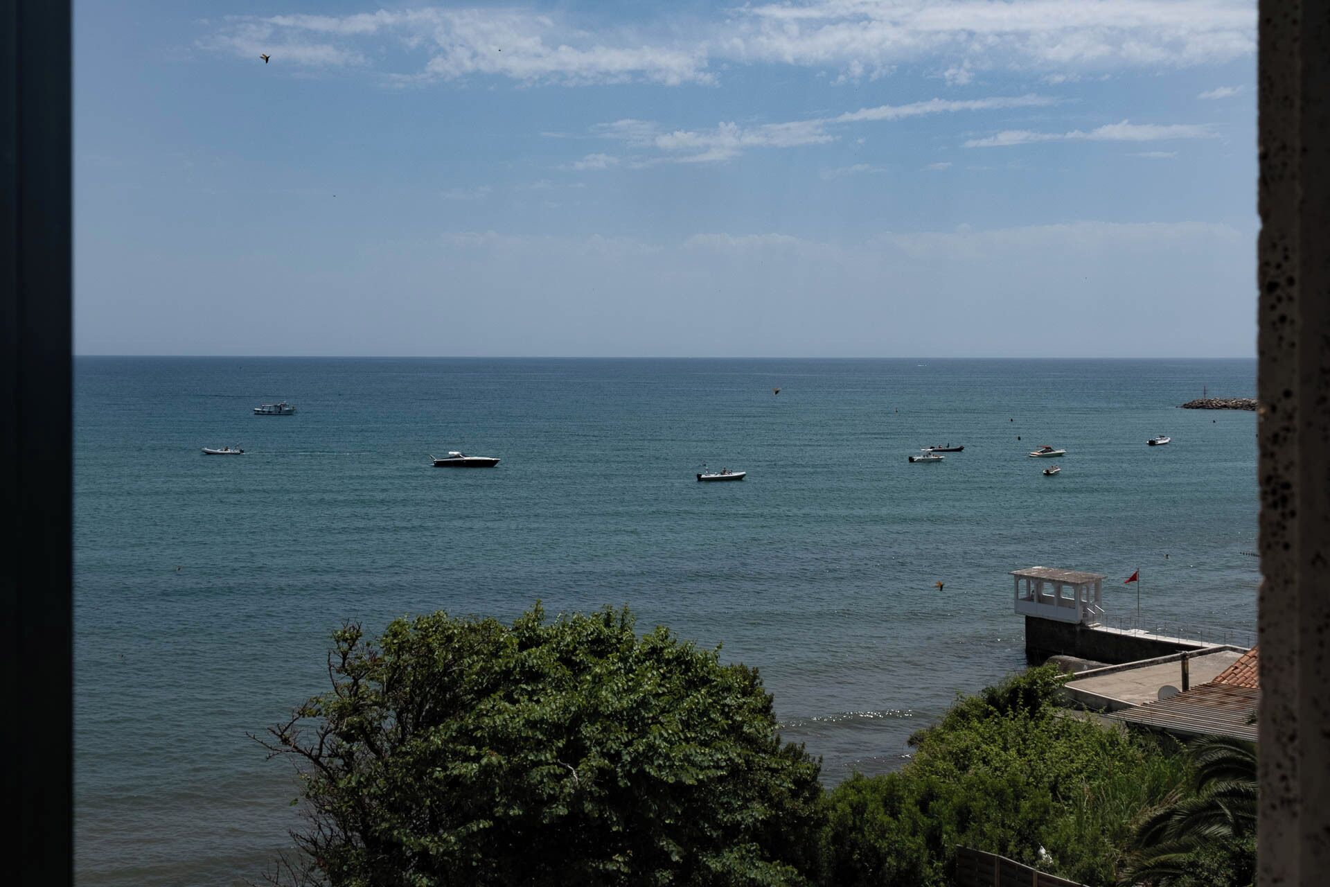 A view of a calm sea with several boats and a small dock with a lifebuoy.