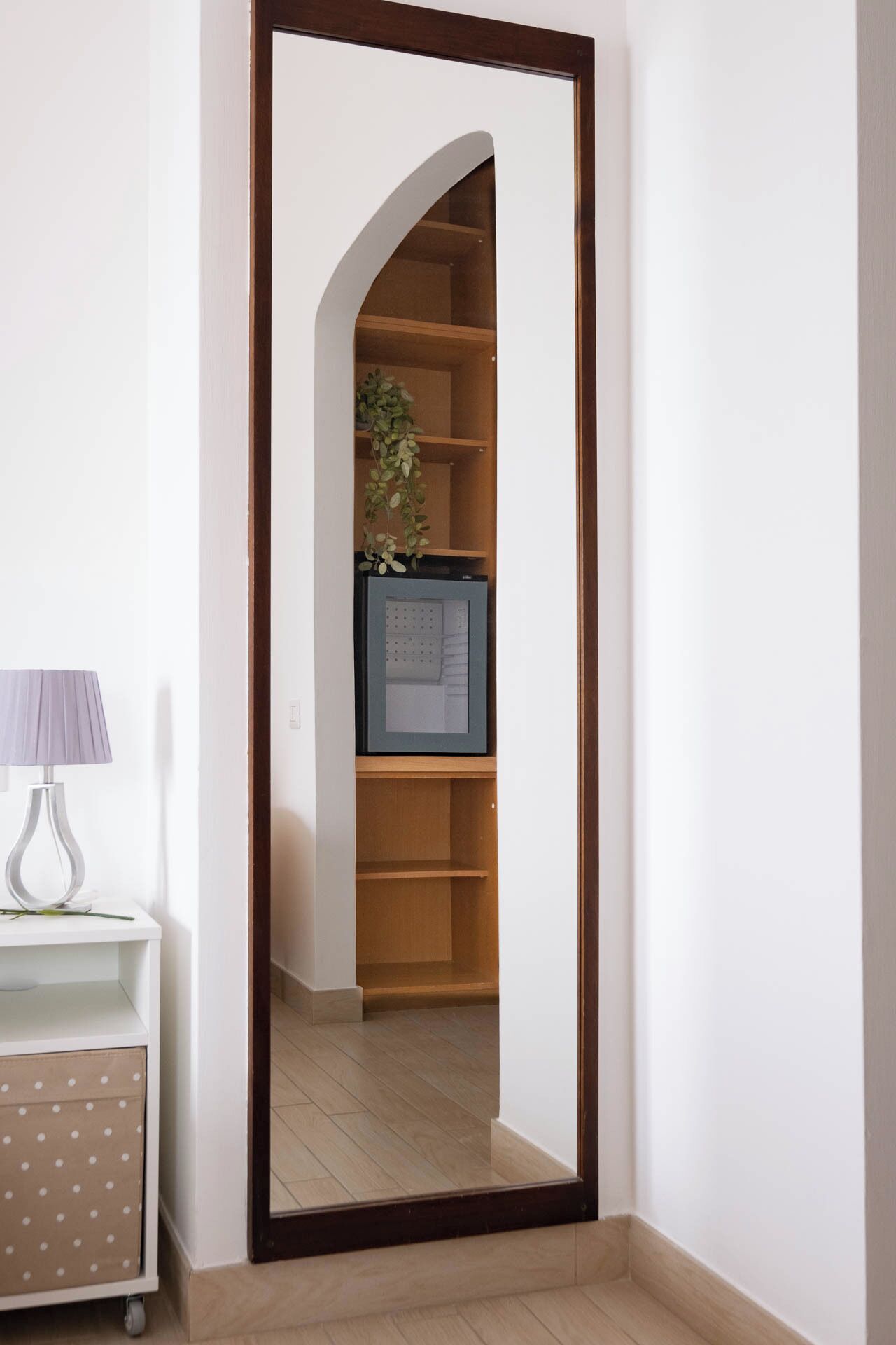 Un corridoio stretto con una porta in legno che dà su una stanza con pavimento in legno e un quadro appeso al muro.