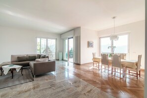 A spacious living room with a sofa, a dining table with chairs, and a view of the outdoors through large windows. - Villa Franco è il posto ideale per una vacanza con la propria famiglia. (Como)