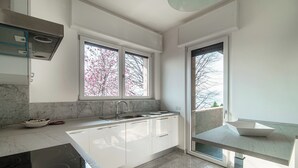 A modern kitchen with white cabinets, a built-in oven, and a window with a view of trees.