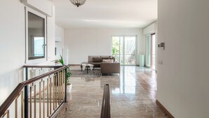 A spacious living room with a large window, a chandelier, and a staircase leading to another level.