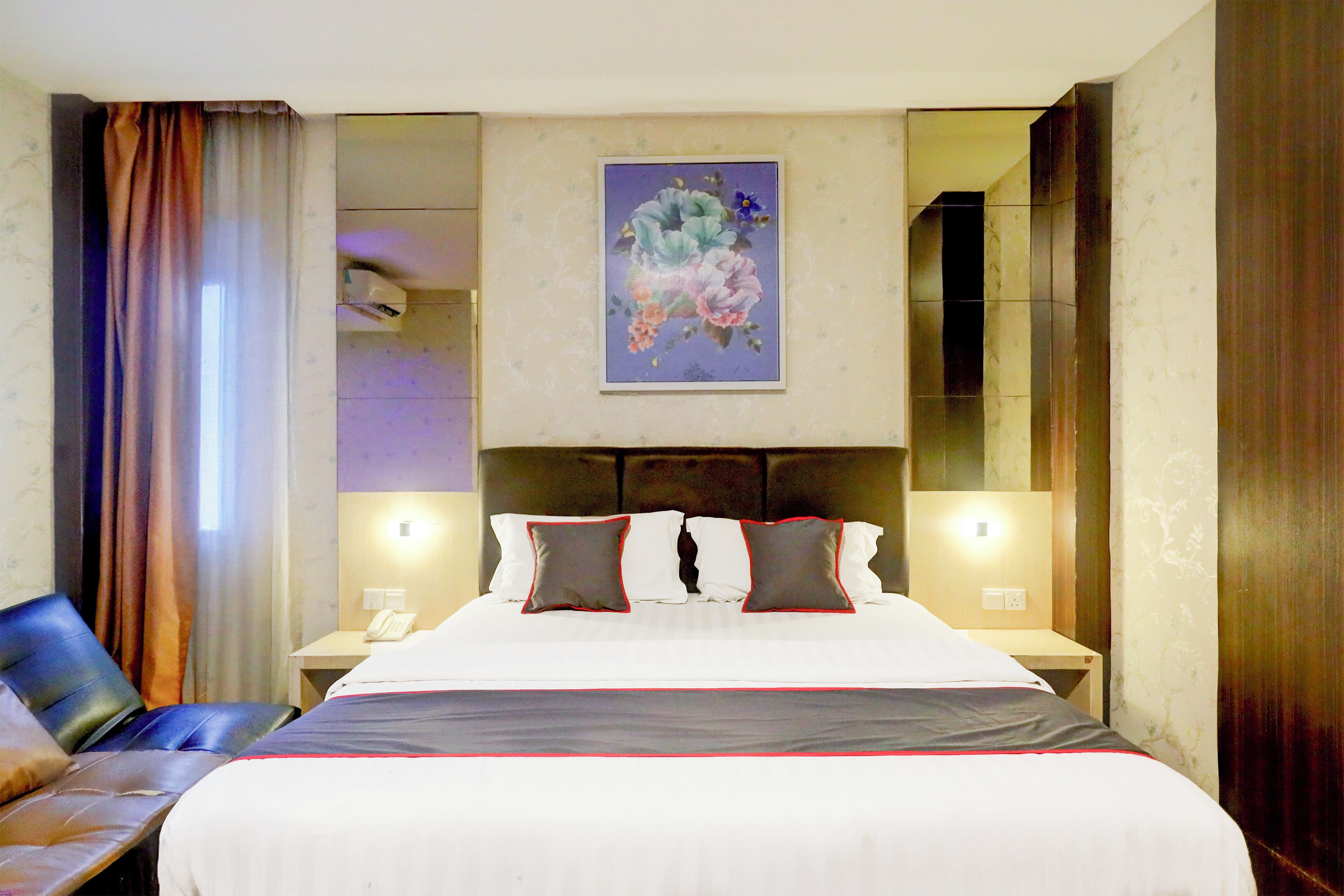 Habitación de hotel con una cama grande, dos mesitas de noche, una silla, un cuadro en la pared y un espejo.