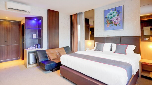 Una habitación de hotel moderna con una cama grande, un área de descanso con sofá y reposapiés, un armario empotrado y un equipo de aire acondicionado de pared.