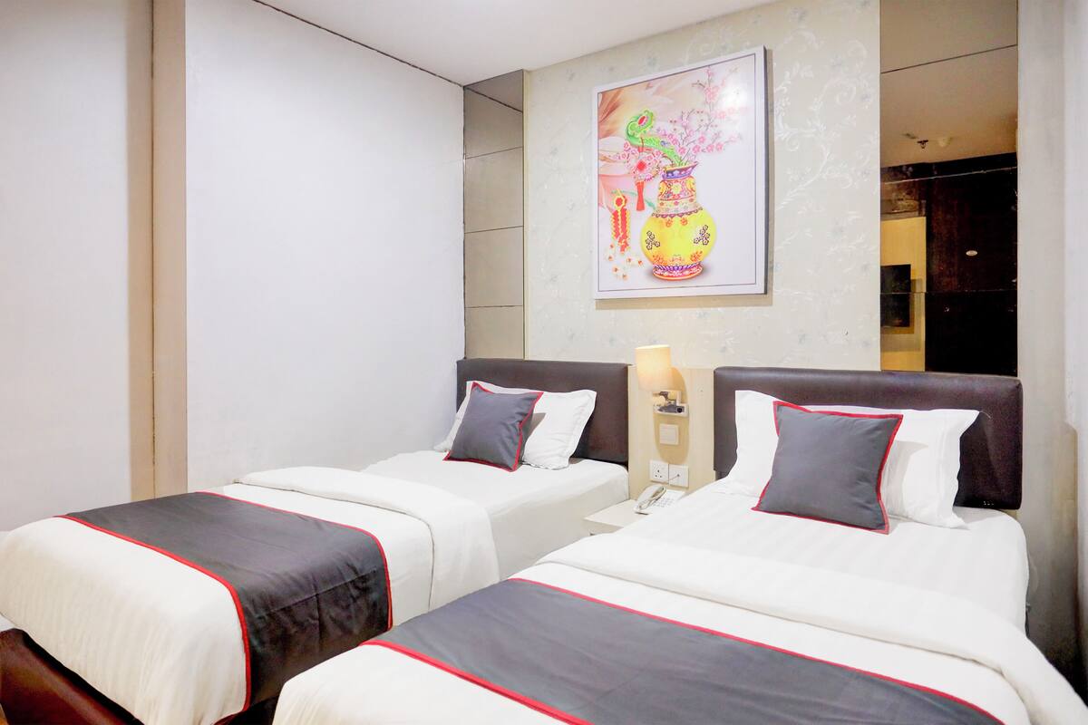 A hotel room with two beds, each with a white and red bedspread, a nightstand with a lamp, and a painting on the wall.